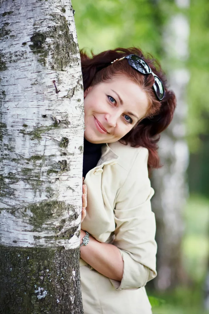 A beautiful woman leans on a Birch tree
