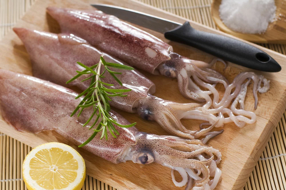 Can Cats Eat Raw Squid:Fresh squids are on a wooden board.